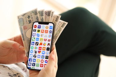 KYIV, UKRAINE - Nisan 1, 2024 Akıllı telefon ekranında birçok uygulama simgesi ve kadın elinde para. Uygulama logosu ve Japon Yen 'i olan iPhone ekranı kadınların elinde. Kapatın.