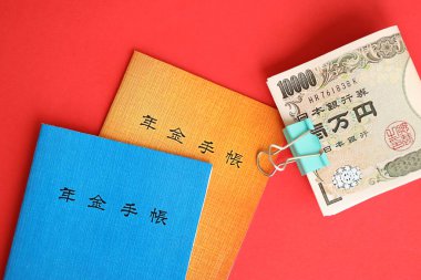 Japon emeklilik sigortası broşürleri yen para faturalarıyla dolu masada. Japon emekliler için mavi ve turuncu kitaplar kapanıyor.