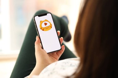 KYIV, UKRAINE - Nisan 1, 2024 Huya simgesi akıllı telefon ekranı kapalı alanda genç kadınların elinde. iPhone uygulaması kullanan kadın