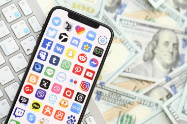 KYIV, UKRAINE - Nisan 1, 2024 Birçok akıllı telefon ekranındaki birçok uygulama simgesi. Uygulama logosuna sahip iPhone görüntüsü ve beyaz klavyeli dolar banknotları