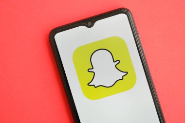 KYIV, UKRAINE - 1 Nisan 2024 Snapchat simgesi kırmızı masadaki akıllı telefon ekranında. Parlak kırmızı arkaplanda uygulama logosuna sahip iPhone görüntüsü