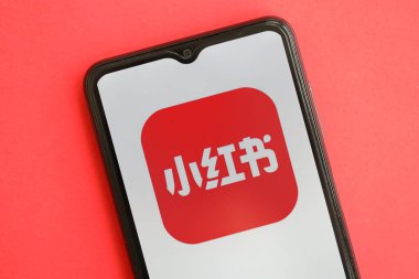 KYIV, UKRAINE - 1 Nisan 2024 Xiaohongshu simgesi kırmızı masadaki akıllı telefon ekranında. Parlak kırmızı arkaplanda uygulama logosuna sahip iPhone görüntüsü