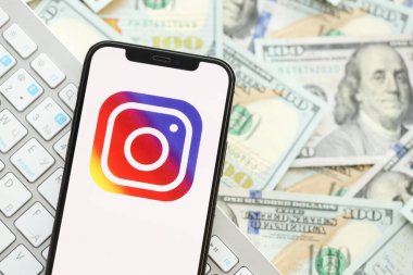 KYIV, UKRAINE - Nisan 1, 2024 Instagram simgesi birçok kullanım parasında akıllı telefon ekranında. Uygulama logosuna sahip iPhone görüntüsü ve beyaz klavyeli dolar banknotları