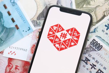 KYIV, UKRAINE - 1 Nisan 2024 Pinduoduo simgesi birçok Asya para bankasında akıllı telefon ekranında. Japon yen ve Çin Yuan banknotları içeren uygulamalı iPhone ekranı