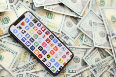 KYIV, UKRAINE - Nisan 1, 2024 Akıllı telefon ekranında birçok uygulama simgesi ve birçok kullanım parası. Uygulama logolu iPhone görüntüsü ve bir sürü yüz dolarlık banknotlar