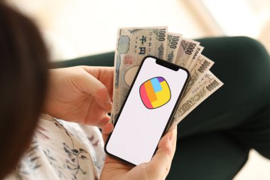 KYIV, UKRAINE - APRIL 1, 2024 Sharechat icon on smartphone screen and money in female hand. iPhone display with app logo and japanese yen money bills in women hands close up clipart