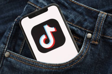 KYIV, UKRAINE - 1 Nisan 2024 TikTok veya Douyin simgesi kot pantolon cebinde akıllı telefon ekranında. Uygulama logosuna sahip iPhone görüntüsü. Moda görünümlü kotların cebinde gizleniyor.