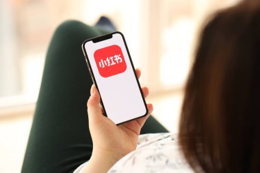 KYIV, UKRAINE - Nisan 1, 2024 Xiaohongshu simgesi akıllı telefon ekranında, kapalı alanda genç kadınların elinde. iPhone uygulaması kullanan kadın