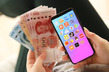 KYIV, UKRAINE - Nisan 1, 2024 Asya uygulama simgesi akıllı telefon ekranında ve kadın elinde para. Uygulama logolu iPhone ekranı ve Çin Yuan 'ı kadınların elinde. Kapatın.