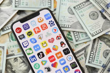 KYIV, UKRAINE - Nisan 1, 2024 Akıllı telefon ekranında birçok uygulama simgesi ve birçok kullanım parası. Uygulama logolu iPhone görüntüsü ve bir sürü yüz dolarlık banknotlar