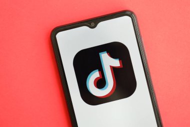KYIV, UKRAINE - Nisan 1, 2024 TikTok veya Douyin simgesi kırmızı masadaki akıllı telefon ekranında. Parlak kırmızı arkaplanda uygulama logosuna sahip iPhone görüntüsü