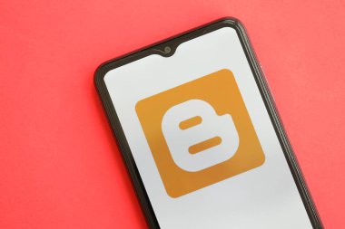 KYIV, UKRAINE - Nisan 1, 2024 Blogger simgesi kırmızı masadaki akıllı telefon ekranında. Parlak kırmızı arkaplanda uygulama logosuna sahip iPhone görüntüsü