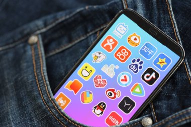KYIV, UKRAINE - 1 Nisan 2024 Asya uygulama simgesi akıllı telefon ekranında kot pantolon cebinde. Uygulama logosuna sahip iPhone görüntüsü. Moda görünümlü kotların cebinde gizleniyor.