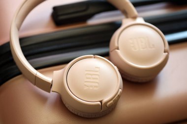 KYIV, UKRAINE - 20 Nisan 2024 JBL Tune 500bt hafif şeftali rengi kulaklıklar yolcuların bagaj çantasına yakın yatar