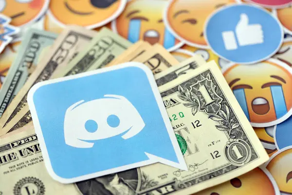 stock image KYIV, UKRAINE - APRIL 20, 2024 Discord logo and many usd money bills. Symbol of famous social network platform and dollar currency banknotes on lot of emoji reactions close up