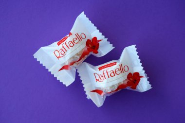 KYIV, UKRAINE - 20 Nisan 2024 Ferrero Raffaello premium tatlılar İtalyan çikolata üreticisi Ferrero SpA tarafından mor arka planda üretildi. Raffaello şekerlemeleri küresel bir hindistan cevizi badem şekerlemesidir.