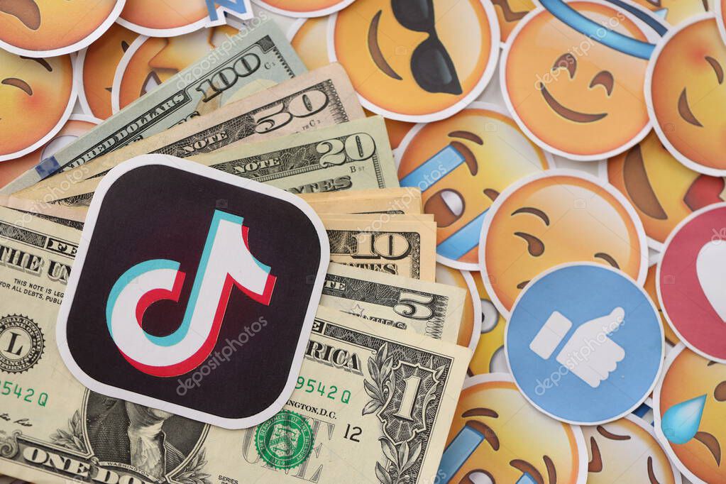 KYIV, UKRAINE - APRIL 20, 2024 TikTok logo and many usd money bills. Symbol of famous social network platform and dollar currency banknotes on lot of emoji reactions close up