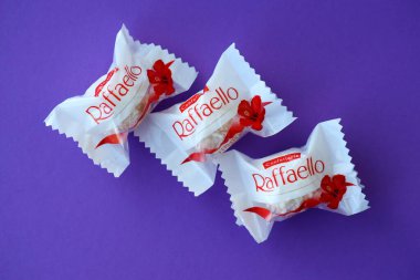 KYIV, UKRAINE - 20 Nisan 2024 Ferrero Raffaello premium tatlılar İtalyan çikolata üreticisi Ferrero SpA tarafından mor arka planda üretildi. Raffaello şekerlemeleri küresel bir hindistan cevizi badem şekerlemesidir.