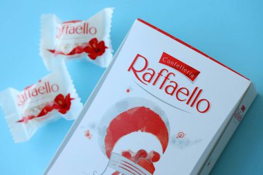 KYIV, UKRAINE - 20 Nisan 2024 Ferrero Raffaello premium tatlılar İtalyan çikolatacı Ferrero SpA tarafından mavi arka planda üretildi. Raffaello şekerlemeleri küresel bir hindistan cevizi badem şekerlemesidir.