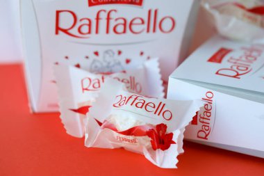 KYIV, UKRAINE - 20 Nisan 2024 Ferrero Raffaello premium tatlılar İtalyan çikolata üreticisi Ferrero SpA tarafından kırmızı arka planda üretildi. Raffaello şekerlemeleri küresel bir hindistan cevizi badem şekerlemesidir.