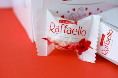 KYIV, UKRAINE - 20 Nisan 2024 Ferrero Raffaello premium tatlılar İtalyan çikolata üreticisi Ferrero SpA tarafından kırmızı arka planda üretildi. Raffaello şekerlemeleri küresel bir hindistan cevizi badem şekerlemesidir.