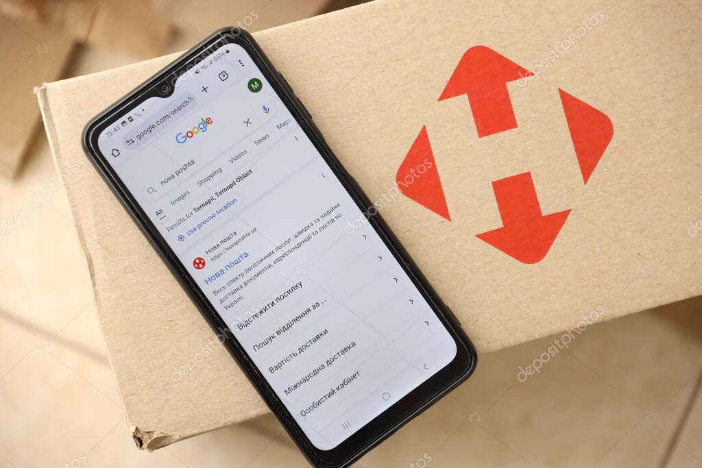 KYIV, UKRAINE - APRIL 20, 2024 Nova Poshta Logotype on cardboard box and website on smartphone display screen. Nova Poshta is best ukrainian postal service company