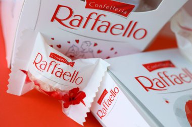 KYIV, UKRAINE - 20 Nisan 2024 Ferrero Raffaello premium tatlılar İtalyan çikolata üreticisi Ferrero SpA tarafından kırmızı arka planda üretildi. Raffaello şekerlemeleri küresel bir hindistan cevizi badem şekerlemesidir.