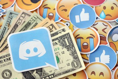 KYIV, UKRAINE - 20 Nisan 2024 Discord logosu ve birçok kullanım dışı para. Birçok emoji reaksiyonuna ilişkin ünlü sosyal ağ platformu ve dolar banknotlarının sembolü