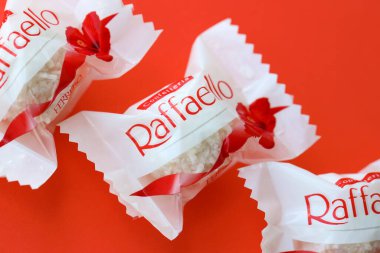 KYIV, UKRAINE - 20 Nisan 2024 Ferrero Raffaello premium tatlılar İtalyan çikolata üreticisi Ferrero SpA tarafından kırmızı arka planda üretildi. Raffaello şekerlemeleri küresel bir hindistan cevizi badem şekerlemesidir.