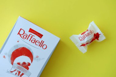 KYIV, UKRAINE - 20 Nisan 2024 Ferrero Raffaello premium tatlılar İtalyan çikolatacı Ferrero SpA tarafından sarı arka planda üretildi. Raffaello şekerlemeleri küresel bir hindistan cevizi badem şekerlemesidir.