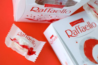 KYIV, UKRAINE - 20 Nisan 2024 Ferrero Raffaello premium tatlılar İtalyan çikolata üreticisi Ferrero SpA tarafından kırmızı arka planda üretildi. Raffaello şekerlemeleri küresel bir hindistan cevizi badem şekerlemesidir.