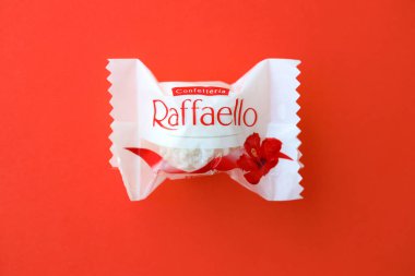 KYIV, UKRAINE - 20 Nisan 2024 Ferrero Raffaello premium tatlılar İtalyan çikolata üreticisi Ferrero SpA tarafından kırmızı arka planda üretildi. Raffaello şekerlemeleri küresel bir hindistan cevizi badem şekerlemesidir.