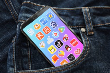 KYIV, UKRAINE - APRIL 1, 2024 Asian apps icon on smartphone display screen in jeans pocket. iPhone display with app logo hide in fashionable denims pocket close up clipart