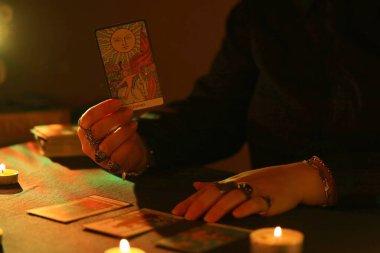 KYIV, UKRAINE - 10 Temmuz 2024 Tarot okuyucusu tarot kartı seçiyor. Karanlık odada mum ışığı. Tarot okuyucusu veya falcı okuma ve tahmin yakın yakın