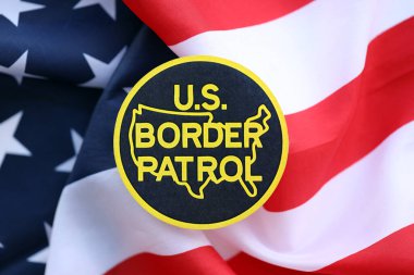 KYIV, UKRAINE - JUNE 26, 2024 U.S. Border Patrol coat of arms sticker on folded US flag close up clipart