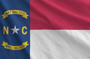 North Carolina US state flag depicted on folded wavy fabric of old cloth close up clipart