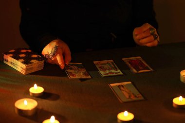 KYIV, UKRAINE - 10 Temmuz 2024 Tarot okuyucusu tarot kartı seçiyor. Karanlık odada mum ışığı. Tarot okuyucusu veya falcı okuma ve tahmin yakın yakın