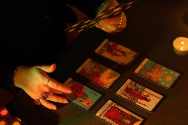 KYIV, UKRAINE - 10 Temmuz 2024 Tarot okuyucusu tarot kartı seçiyor. Karanlık odada mum ışığı. Tarot okuyucusu veya falcı okuma ve tahmin yakın yakın