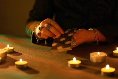 KYIV, UKRAINE - 10 Temmuz 2024 Tarot okuyucusu tarot kartı seçiyor. Karanlık odada mum ışığı. Tarot okuyucusu veya falcı okuma ve tahmin yakın yakın