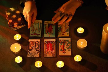 KYIV, UKRAINE - 10 Temmuz 2024 Tarot okuyucusu tarot kartı seçiyor. Karanlık odada mum ışığı. Tarot okuyucusu veya falcı okuma ve tahmin yakın yakın