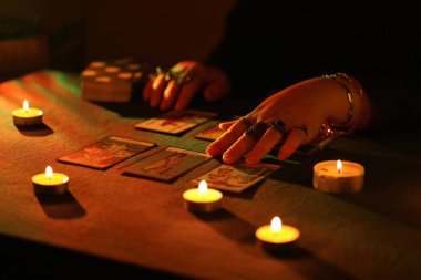 KYIV, UKRAINE - 10 Temmuz 2024 Tarot okuyucusu tarot kartı seçiyor. Karanlık odada mum ışığı. Tarot okuyucusu veya falcı okuma ve tahmin yakın yakın