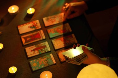 KYIV, UKRAINE - 10 Temmuz 2024 Tarot okuyucusu tarot kartı seçiyor. Karanlık odada mum ışığı. Tarot okuyucusu veya falcı okuma ve tahmin yakın yakın