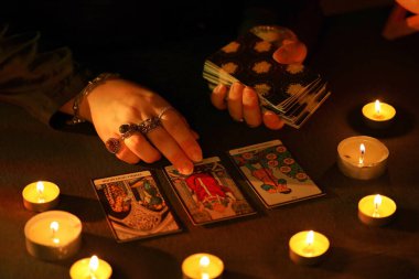 KYIV, UKRAINE - 10 Temmuz 2024 Tarot okuyucusu tarot kartı seçiyor. Karanlık odada mum ışığı. Tarot okuyucusu veya falcı okuma ve tahmin yakın yakın