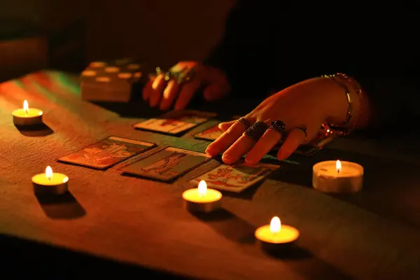 stock image KYIV, UKRAINE - JULY 10, 2024 Tarot reader picking tarot cards. Candlelight in dark room. Tarot reader or fortune teller reading and forecasting close up