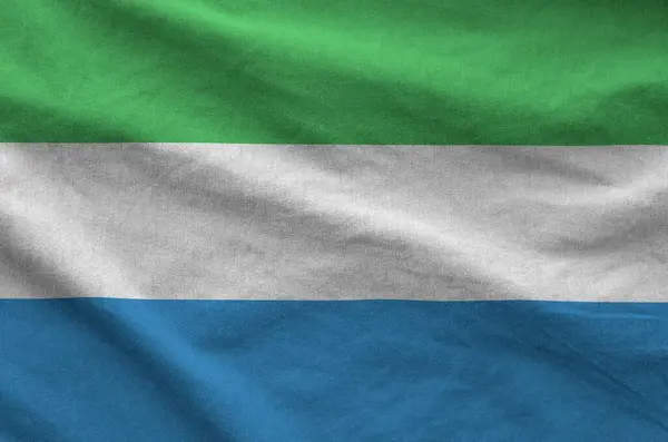 stock image Sierra Leone flag depicted on folded wavy fabric of old cloth close up