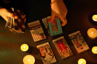 KYIV, UKRAINE - 10 Temmuz 2024 Tarot okuyucusu tarot kartı seçiyor. Karanlık odada mum ışığı. Tarot okuyucusu veya falcı okuma ve tahmin yakın yakın