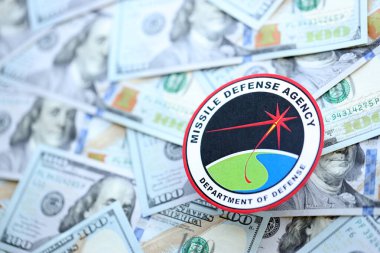 KYIV, UKRAINE - JUNE 26, 2024 Department of Defense Missile Defense Agency coat of arms on big amount of US dollar banknotes close up clipart