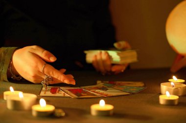KYIV, UKRAINE - 10 Temmuz 2024 Tarot okuyucusu tarot kartı seçiyor. Karanlık odada mum ışığı. Tarot okuyucusu veya falcı okuma ve tahmin yakın yakın