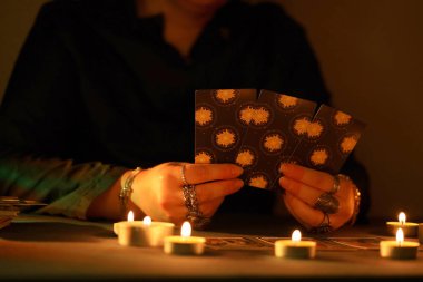 KYIV, UKRAINE - 10 Temmuz 2024 Tarot okuyucusu tarot kartı seçiyor. Karanlık odada mum ışığı. Tarot okuyucusu veya falcı okuma ve tahmin yakın yakın