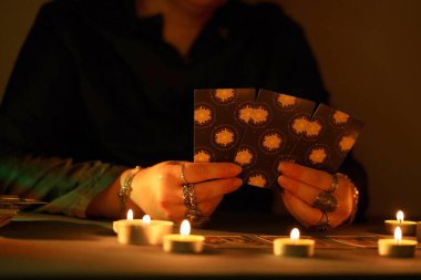 KYIV, UKRAINE - JULY 10, 2024 Tarot reader picking tarot cards. Candlelight in dark room. Tarot reader or fortune teller reading and forecasting close up clipart